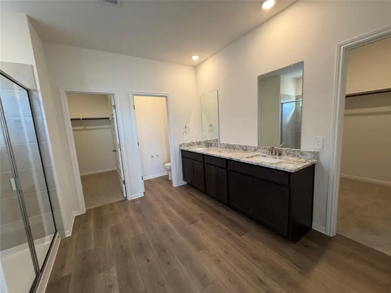 Full bath featuring a walk in closet, a shower stall, double vanity, dark wood-type flooring, and recessed lighting Full bath featuring a walk in closet, a shower stall, double vanity, dark wood-type flooring, and recessed lighting