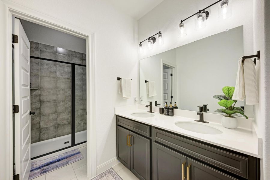 Full bath with a shower stall, double vanity, and light tile patterned floors