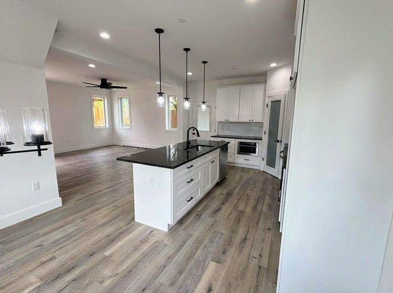 Kitchen with open floor plan, white cabinetry, pendant lighting, and dark stone counters