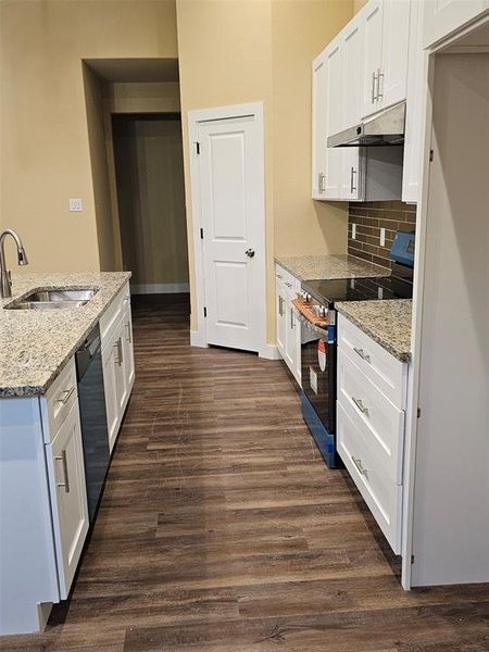 Kitchen with light stone countertops, white cabinetry, stainless steel electric range oven, sink, and dark hardwood / wood-style floors