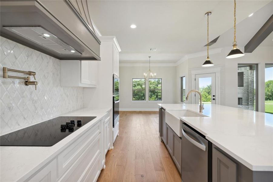 Kitchen with white cabinetry, black appliances, light wood-type flooring, backsplash, and a kitchen island with sink