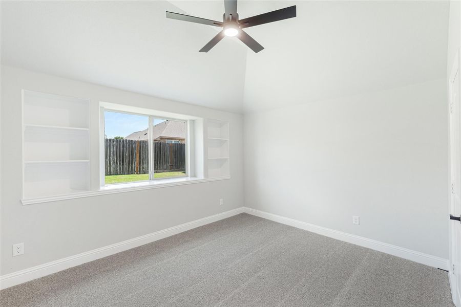 Empty bedroom with vaulted ceiling, ceiling fan, built-in shelves, and carpet flooring Empty bedroom with vaulted ceiling, ceiling fan, built-in shelves, and carpet flooring
