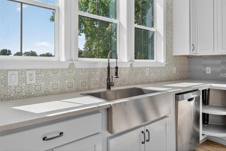 Kitchen with white cabinets, stainless steel dishwasher, backsplash, light stone countertops, and healthy amount of natural light