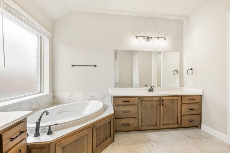 Master bathroom with soaking tub, wood vanity, white countertop, and large mirror with wall lighting Master bathroom with soaking tub, wood vanity, white countertop, and large mirror with wall lighting