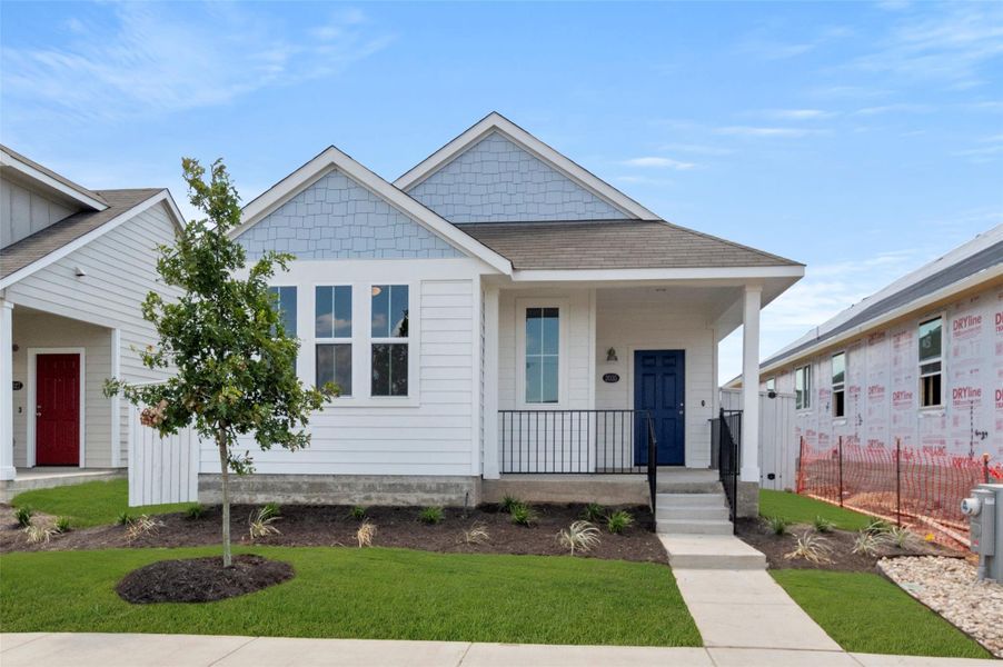 View of front facade with a front yard, a shingled roof, and covered porch