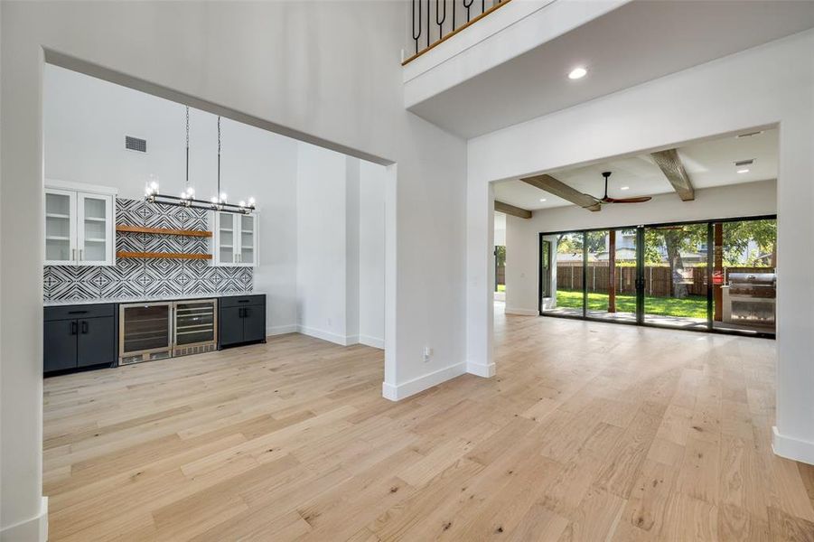 Indoor dry bar featuring dark cabinets, beamed ceiling, light wood finished floors, glass insert cabinets, and decorative backsplash Indoor dry bar featuring dark cabinets, beamed ceiling, light wood finished floors, glass insert cabinets, and decorative backsplash