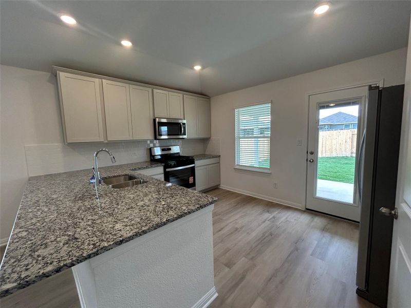 Kitchen featuring dark stone countertops, backsplash, appliances with stainless steel finishes, light wood-type flooring, and recessed lighting Kitchen featuring dark stone countertops, backsplash, appliances with stainless steel finishes, light wood-type flooring, and recessed lighting