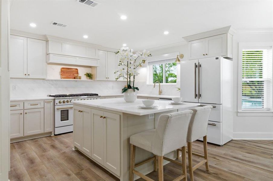 The kitchen features light-colored cabinetry, a large kitchen island with seating, a white refrigerator, and a gas range The kitchen features light-colored cabinetry, a large kitchen island with seating, a white refrigerator, and a gas range