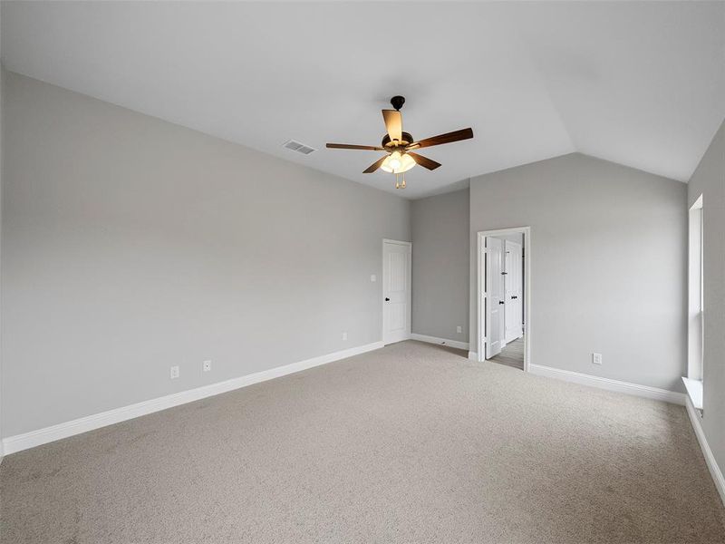 Carpeted spare room featuring visible vents, baseboards, a ceiling fan, and vaulted ceiling