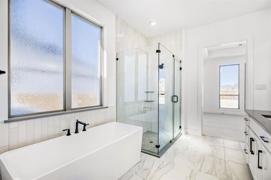 Full bath featuring a stall shower, a freestanding tub, light marble finish floors, and vanity
