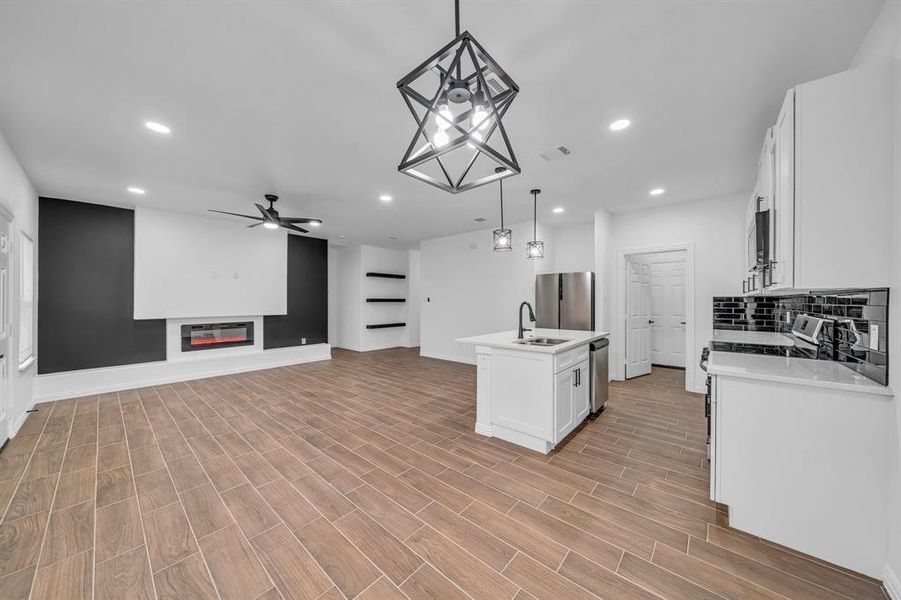 Kitchen with appliances with stainless steel finishes, decorative light fixtures, white cabinetry, an island with sink, and sink