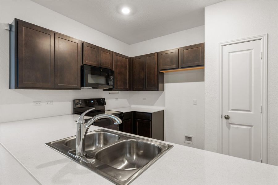 Kitchen with black appliances, dark brown cabinetry, and light countertops Kitchen with black appliances, dark brown cabinetry, and light countertops