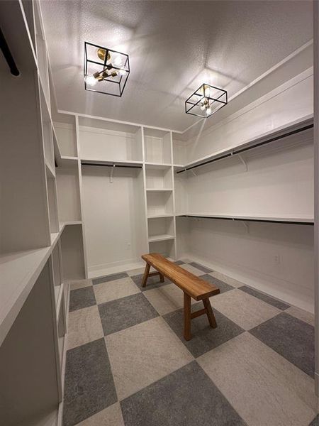Spacious custom closet featuring extensive built-in shelving, hanging rods, two modern flush-mount light fixtures, and checkerboard pattern flooring