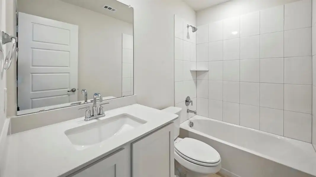 Contemporary bathroom featuring a white vanity with an integrated sink and chrome faucet, a large frameless mirror, a white paneled door, and a shower-over-tub combination with white subway tile surround Contemporary bathroom featuring a white vanity with an integrated sink and chrome faucet, a large frameless mirror, a white paneled door, and a shower-over-tub combination with white subway tile surround