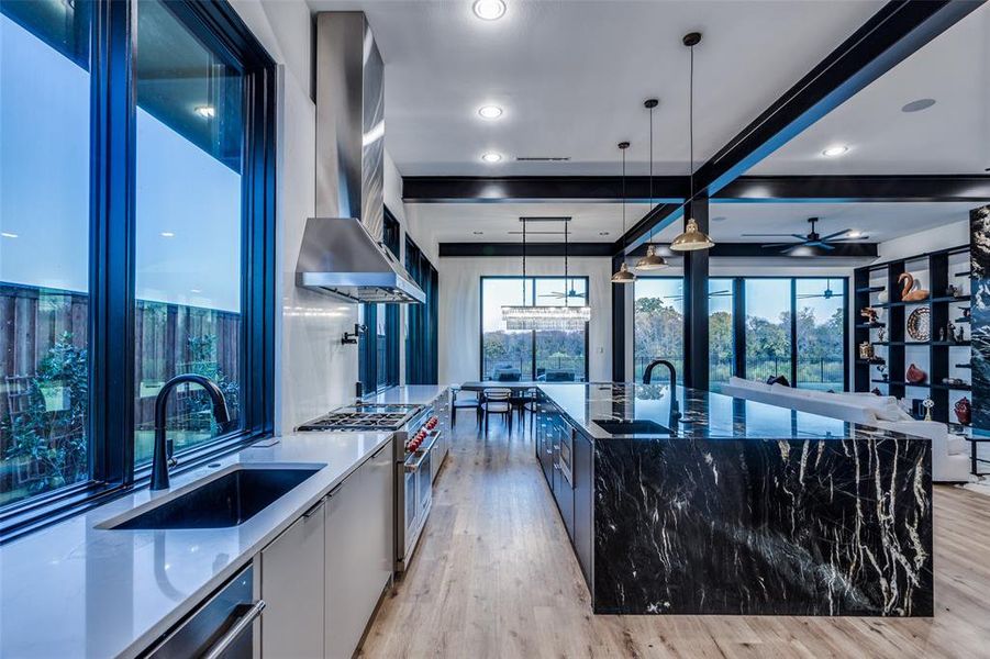 Kitchen featuring wall chimney exhaust hood, decorative light fixtures, a spacious island, and dark stone countertops