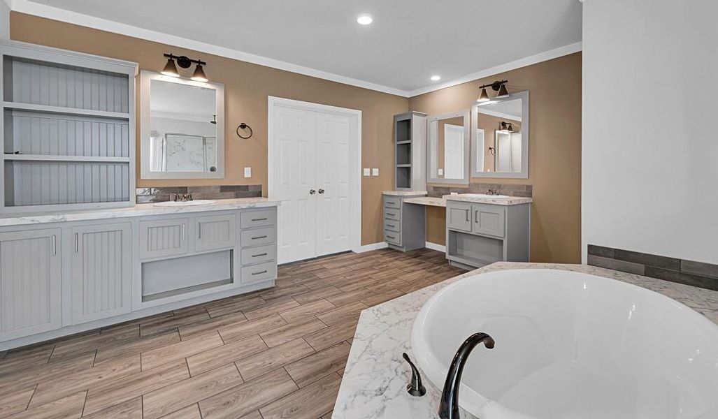 Full bathroom with ornamental molding, two vanities, light wood finished floors, recessed lighting, and a bath Full bathroom with ornamental molding, two vanities, light wood finished floors, recessed lighting, and a bath