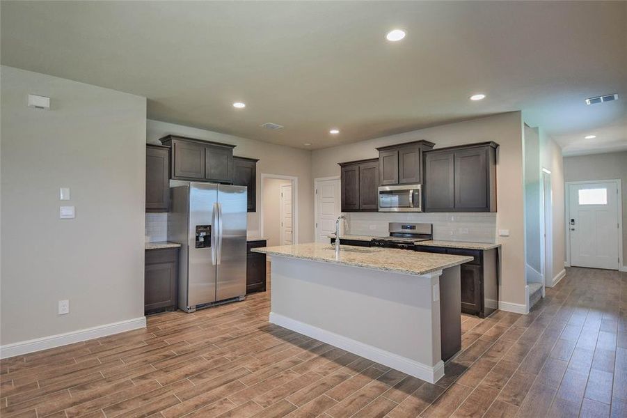 Kitchen featuring stainless steel appliances, light wood-style floors, tasteful backsplash, light stone countertops, and recessed lighting Kitchen featuring stainless steel appliances, light wood-style floors, tasteful backsplash, light stone countertops, and recessed lighting