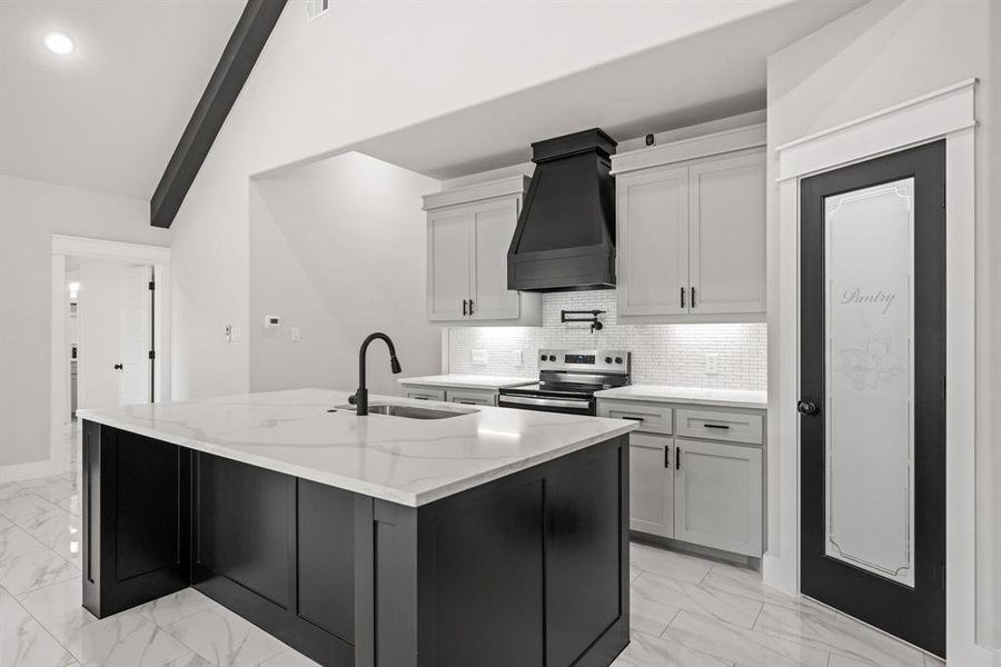 Kitchen featuring dark cabinets, a kitchen island with sink, light stone countertops, and light marble finish flooring