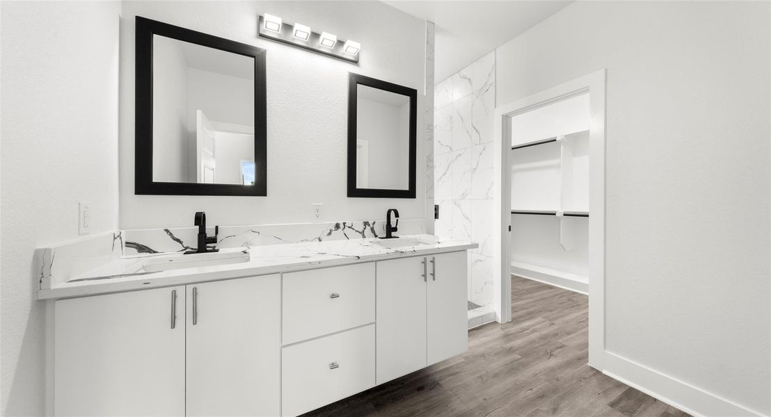 Full bath with double vanity, a walk in closet, and dark wood finished floors