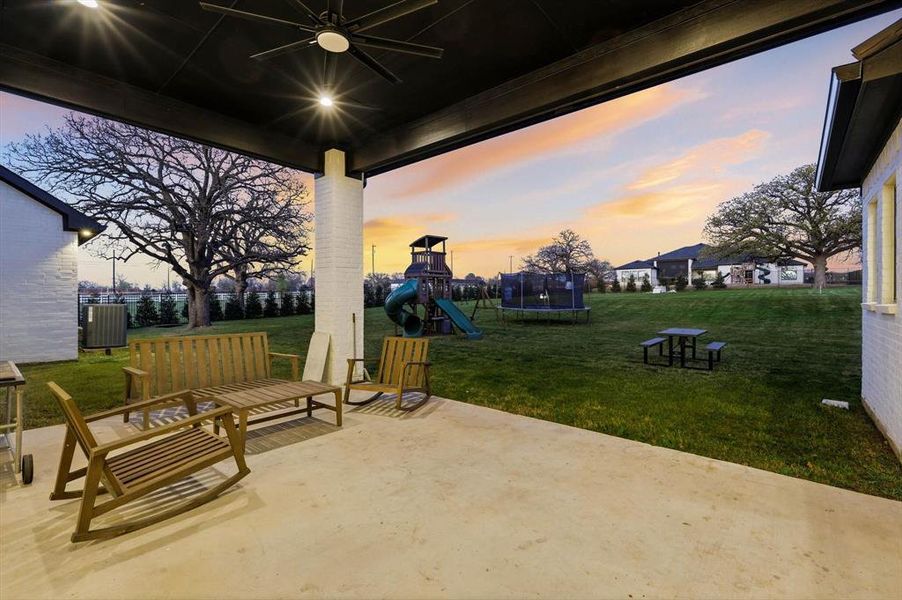 Patio terrace at dusk with a trampoline, a patio, a playground, and a ceiling fan