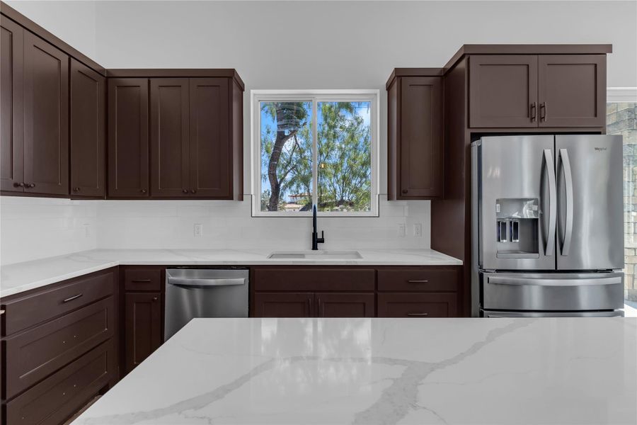 Rich dark wood cabinetry pairs with sleek stone countertops framing a view of mature trees.