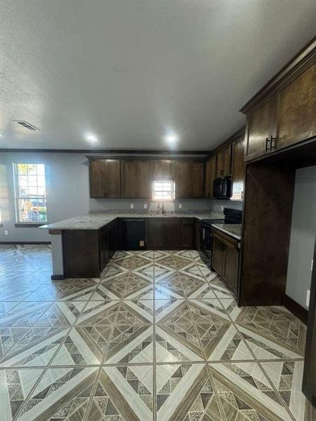 Kitchen featuring dark brown cabinetry, black appliances, light stone countertops, and a peninsula