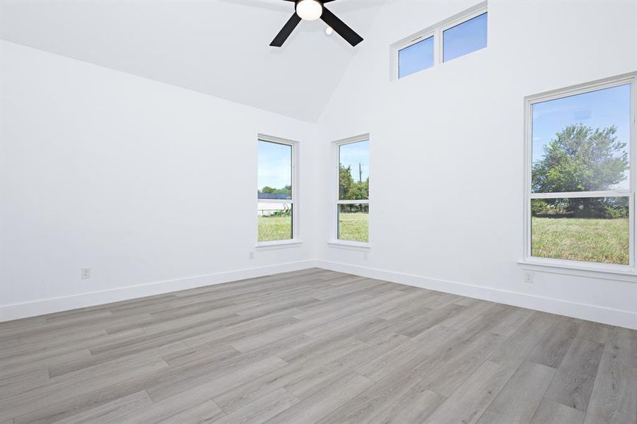 Spare room featuring plenty of natural light, high vaulted ceiling, light wood-style flooring, and a ceiling fan