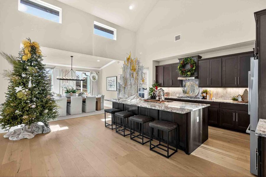 Kitchen with light stone counters, a breakfast bar, plenty of natural light, light wood-style flooring, and high vaulted ceiling