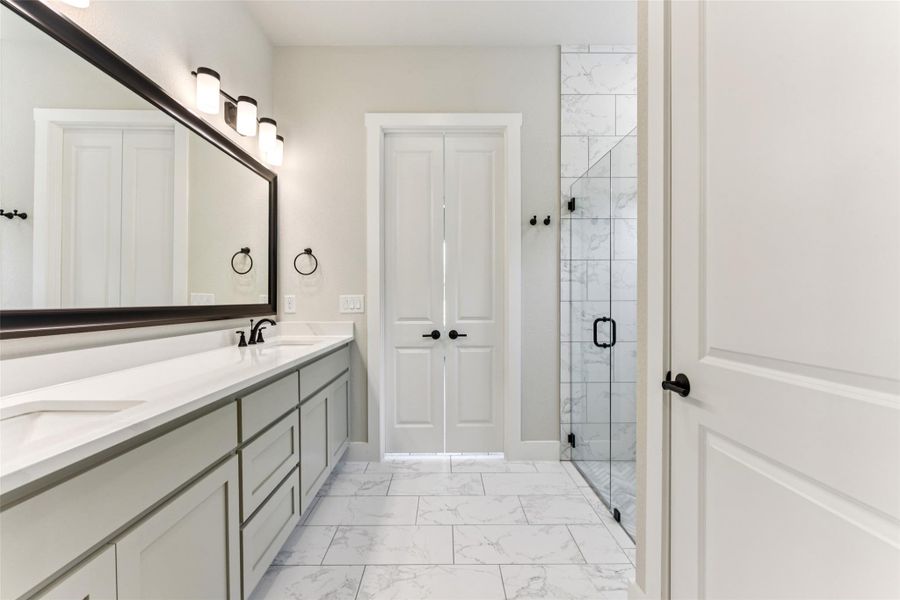 Bathroom featuring a shower stall, double vanity, and light marble finish floors Bathroom featuring a shower stall, double vanity, and light marble finish floors