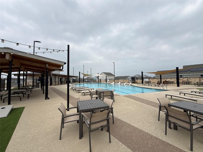 Community swimming pool featuring an expansive paved deck, shaded lounge areas, and string lighting