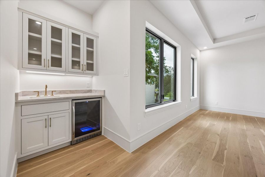A private kitchenette with custom cabinetry, under cabinet lighting, and a beverage refrigerator brings everyday convenience and a touch of luxury to the primary suite. Thoughtfully positioned just outside the bedroom, it creates the perfect space for a morning coffee or evening refreshment.