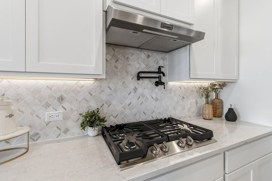 Kitchen cooktop area with stainless steel gas range, white cabinets, marble tile backsplash, and pot filler faucet Kitchen cooktop area with stainless steel gas range, white cabinets, marble tile backsplash, and pot filler faucet