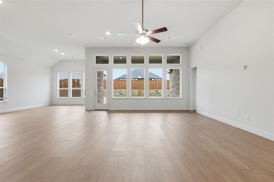 Unfurnished living room featuring light wood-style flooring, ceiling fan, a high ceiling, and recessed lighting