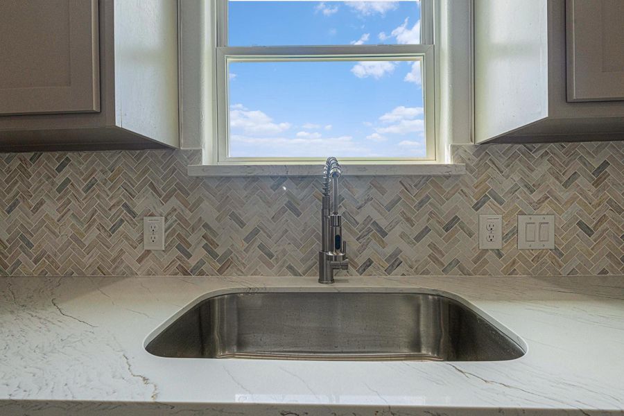 This kitchen features a sleek, modern sink with a stainless steel faucet, set in a marble countertop. The stylish herringbone-patterned backsplash adds elegance, while the window above the sink offers natural light and a view. This kitchen features a sleek, modern sink with a stainless steel faucet, set in a marble countertop. The stylish herringbone-patterned backsplash adds elegance, while the window above the sink offers natural light and a view.