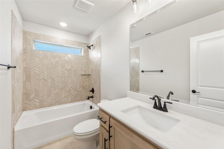 Bathroom with herringbone tile tub surround, white soaking tub, single vanity with quartz countertop, and large mirror