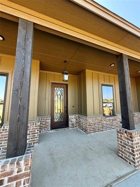 Entrance to property featuring board and batten siding, a porch, and brick siding Entrance to property featuring board and batten siding, a porch, and brick siding