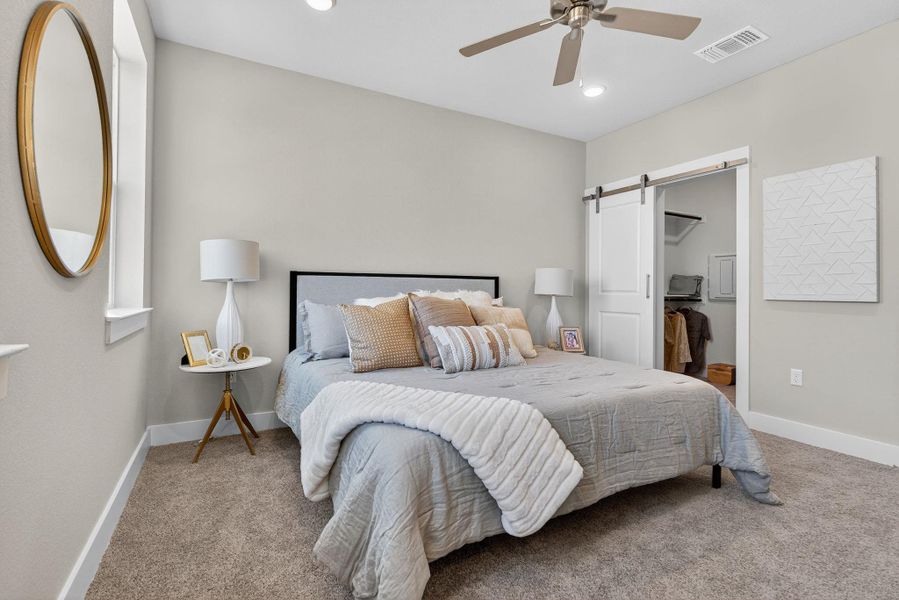 Carpeted bedroom with a barn door, a walk in closet, ceiling fan, and recessed lighting