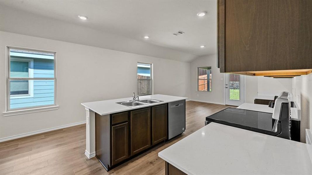 Open-concept kitchen featuring an island with an undermount double-basin sink, quartz countertops, a stainless steel dishwasher, and dark wood-finish cabinetry