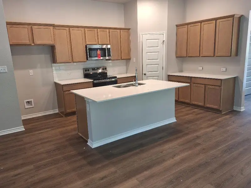 Kitchen with stainless steel appliances, dark wood-type flooring, backsplash, and a center island with sink