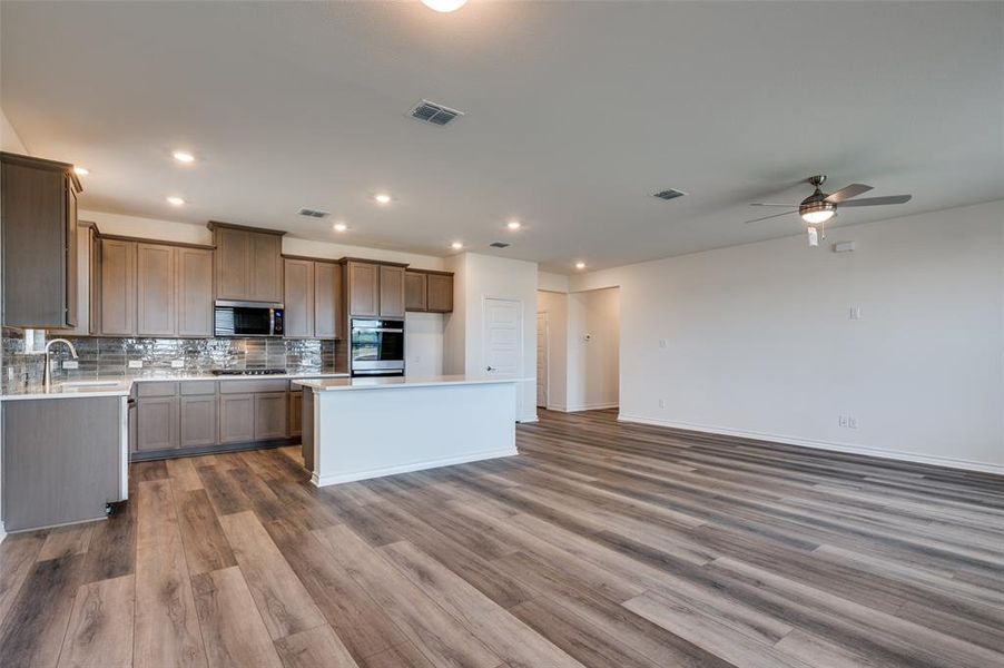 Kitchen featuring dark wood-style floors, a ceiling fan, open floor plan, backsplash, and light countertops Kitchen featuring dark wood-style floors, a ceiling fan, open floor plan, backsplash, and light countertops