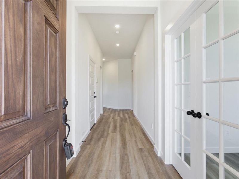 Entryway featuring a paneled wood door with dark hardware, wood-finish flooring, recessed lighting, and a white interior door with glass panes Entryway featuring a paneled wood door with dark hardware, wood-finish flooring, recessed lighting, and a white interior door with glass panes
