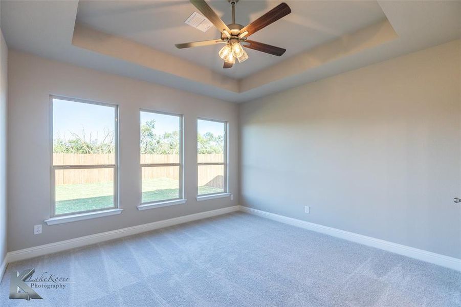 Carpeted empty room with a raised ceiling and a ceiling fan
