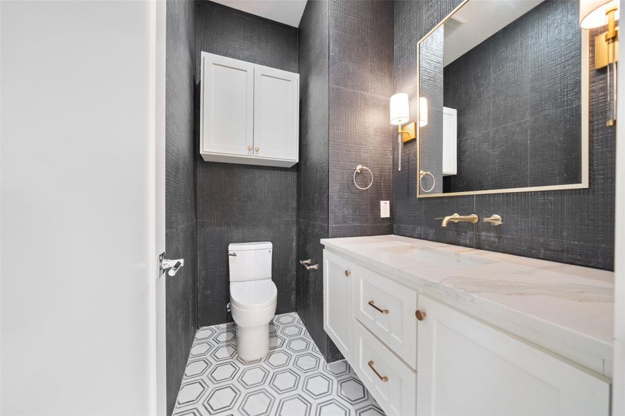 Second floor half bathroom features modern design with dark textured walls, a large mirror, and elegant lighting. It has a stylish white vanity with a marble countertop, a wall-mounted faucet, and hexagonal floor tiles.