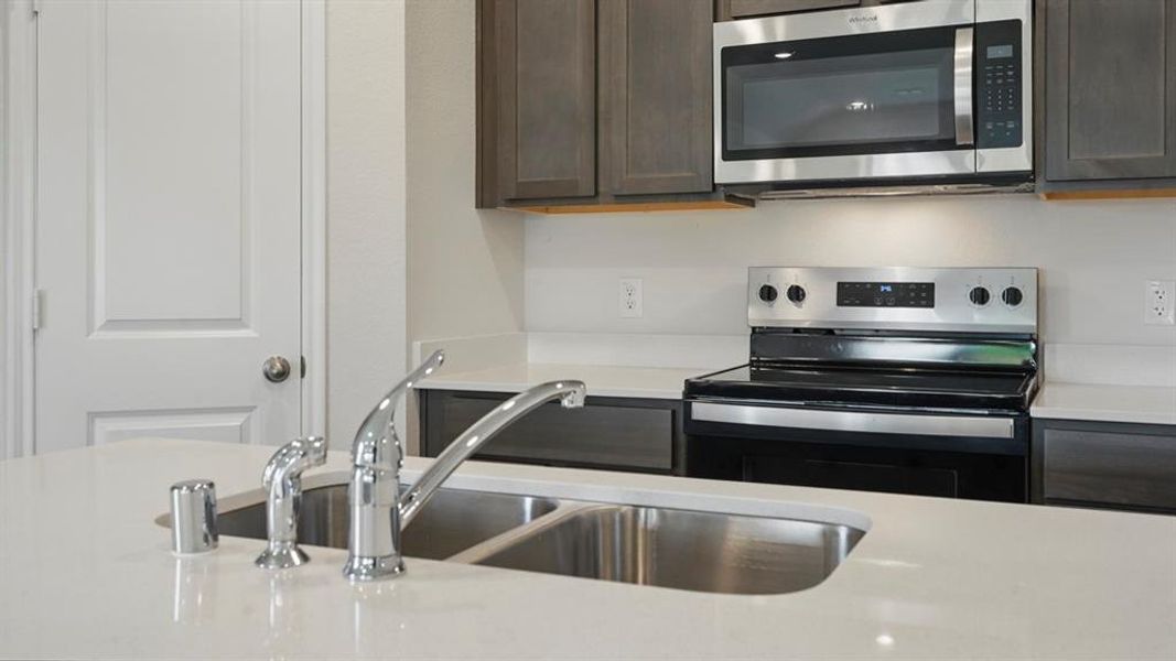 Kitchen with stainless steel appliances, dark brown cabinets, and light stone countertops