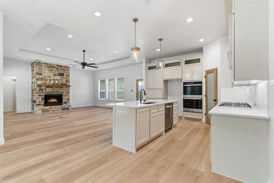 Kitchen with a raised ceiling, a center island with sink, open floor plan, decorative light fixtures, and light wood-type flooring Kitchen with a raised ceiling, a center island with sink, open floor plan, decorative light fixtures, and light wood-type flooring