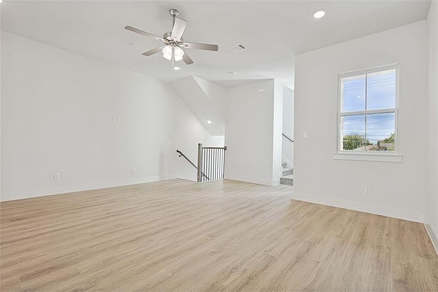 Spacious living area featuring light wood-style flooring, a ceiling fan, and a window providing natural light