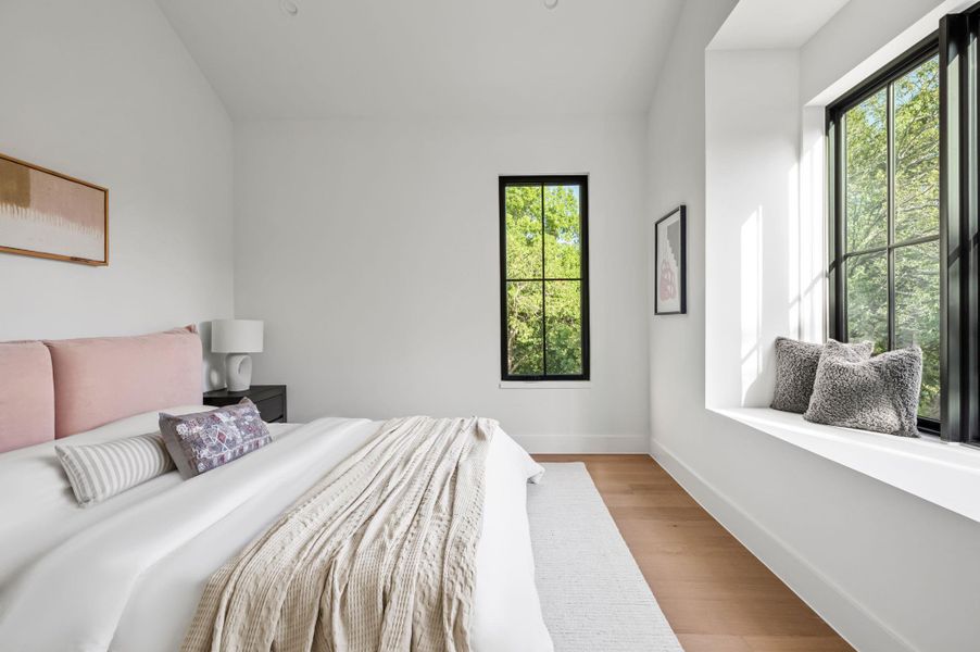 Sun-filled bedroom featuring light wood flooring and a deep window seat with verdant views.