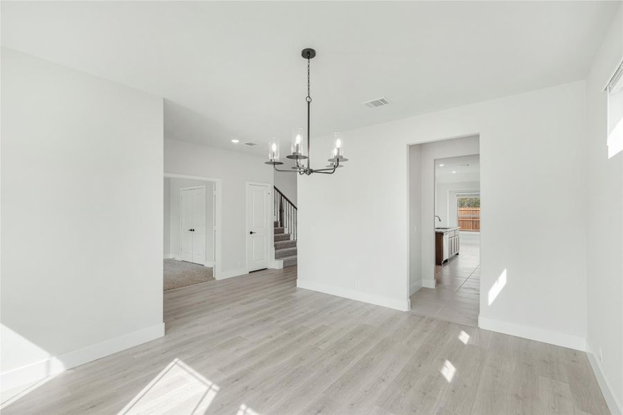 Open dining area with light wood floors, black chandelier, and view of staircase and kitchen