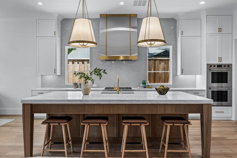 Kitchen featuring an island with sink, light hardwood / wood-style flooring, stainless steel double oven, and tasteful backsplash