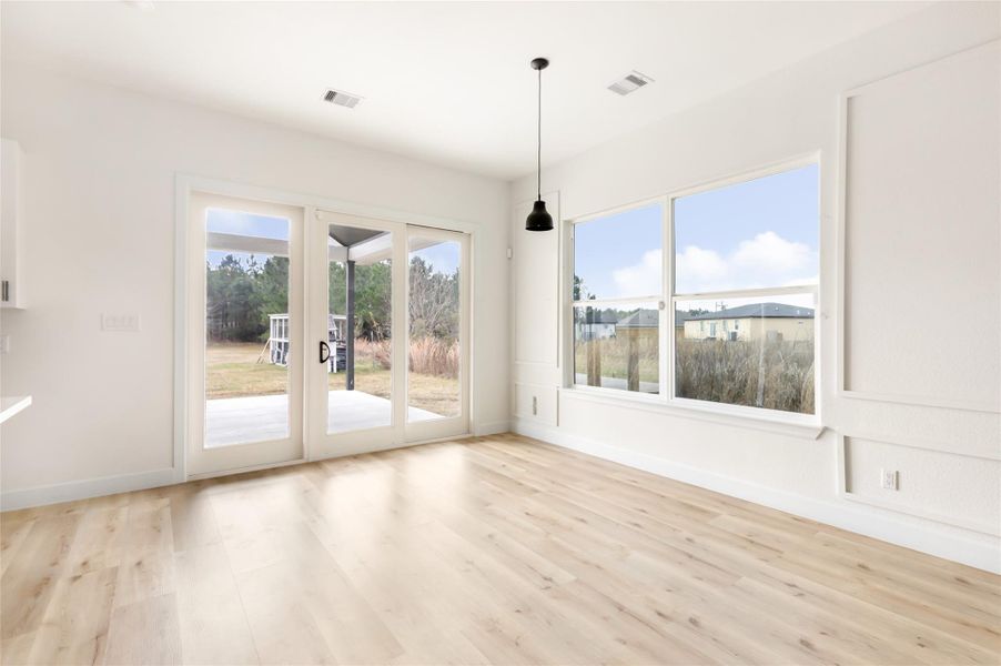 Bright and open room with large windows and sliding glass doors leading to an outdoor patio. Features light wood flooring and a modern pendant light, offering a view of a spacious backyard. Perfect for enjoying natural light and indoor-outdoor living.